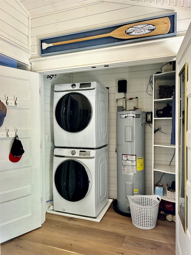 clothes washing area featuring wood-type flooring, electric water heater, stacked washer and dryer, and wood walls