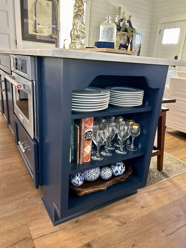 room details with blue cabinetry, stainless steel oven, and light wood-type flooring