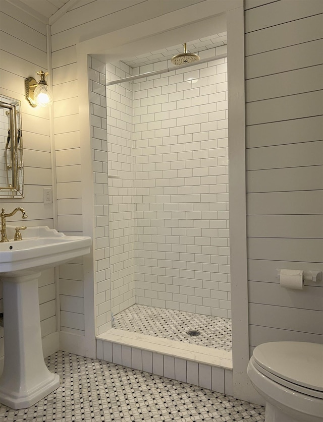 bathroom with a tile shower, wood walls, and toilet