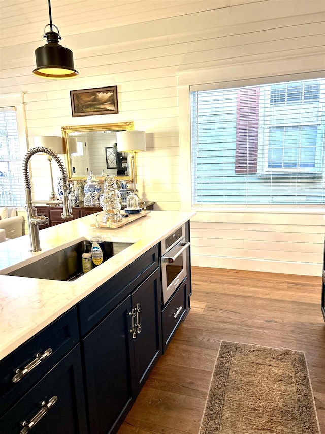 bar featuring pendant lighting, stainless steel oven, dark wood-type flooring, sink, and wooden walls