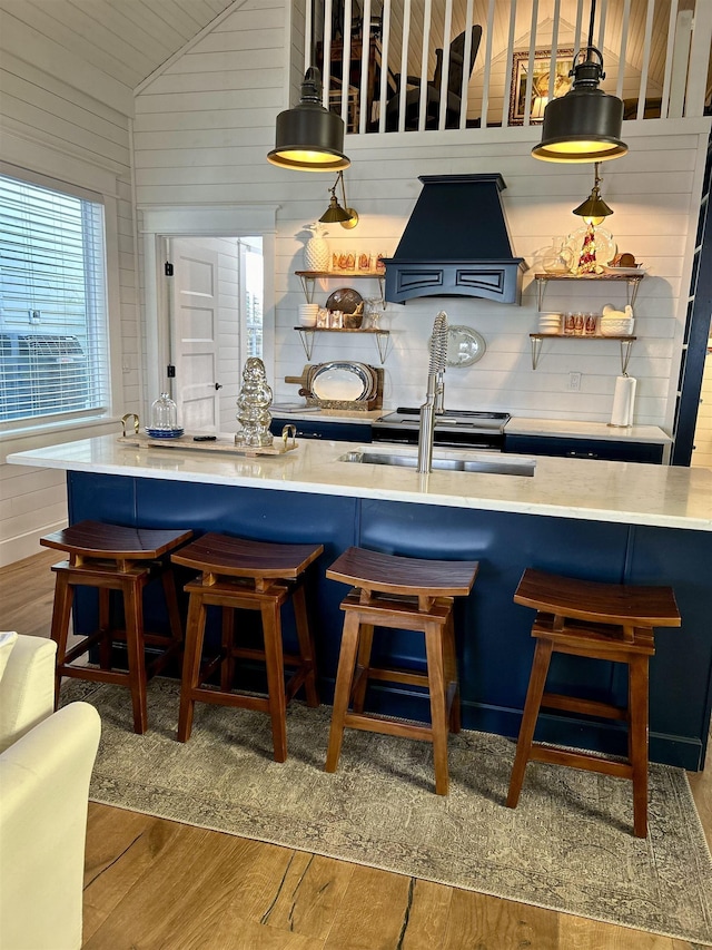 bar featuring lofted ceiling, premium range hood, sink, wooden walls, and wood-type flooring