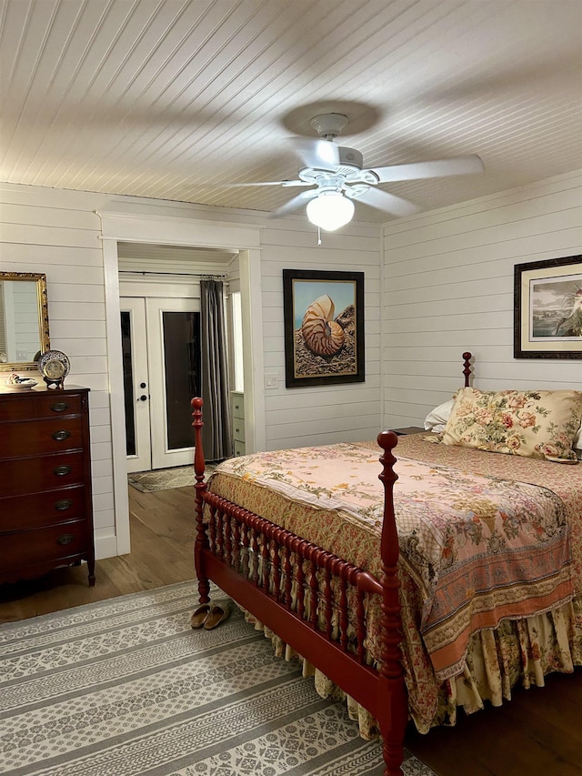 bedroom with french doors, ceiling fan, dark wood-type flooring, and wood walls