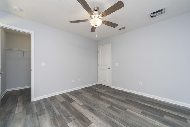 unfurnished bedroom with dark hardwood / wood-style flooring, a walk in closet, a closet, and ceiling fan