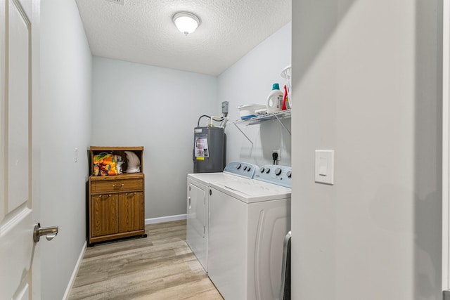 clothes washing area with washer and dryer, electric water heater, a textured ceiling, and light hardwood / wood-style flooring