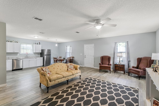 living room featuring ceiling fan, sink, a textured ceiling, and light hardwood / wood-style flooring