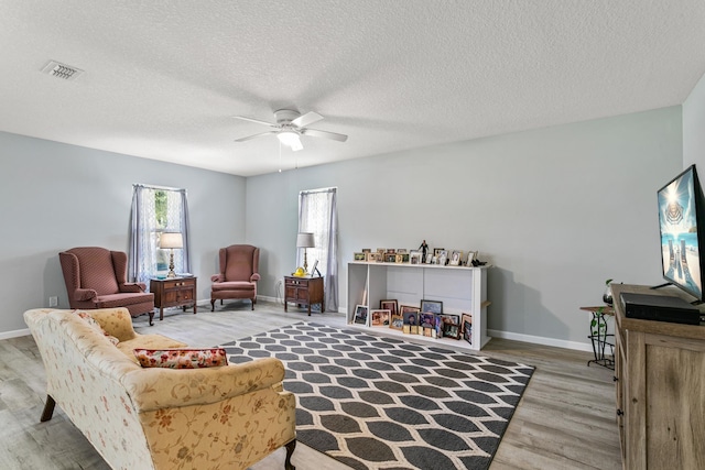 living area featuring ceiling fan, wood-type flooring, and a textured ceiling