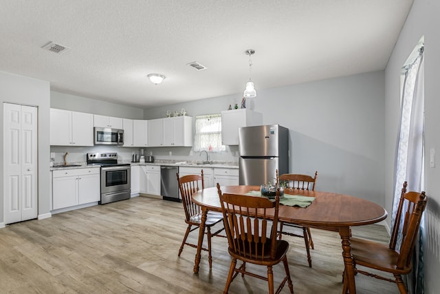 kitchen with white cabinets, decorative light fixtures, stainless steel appliances, and light hardwood / wood-style flooring