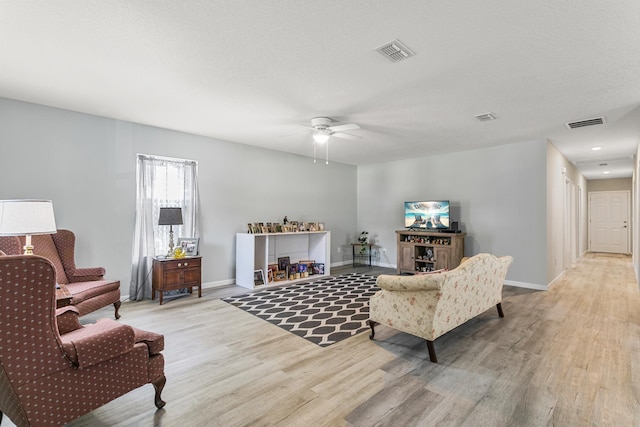 living room featuring ceiling fan, light hardwood / wood-style floors, and a textured ceiling