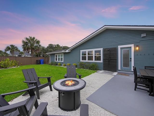 patio terrace at dusk with a lawn, a fire pit, and fence