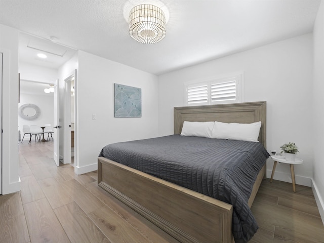 bedroom with light wood-type flooring, attic access, and baseboards