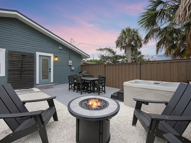 patio terrace at dusk with an outdoor fire pit, outdoor dining area, and fence