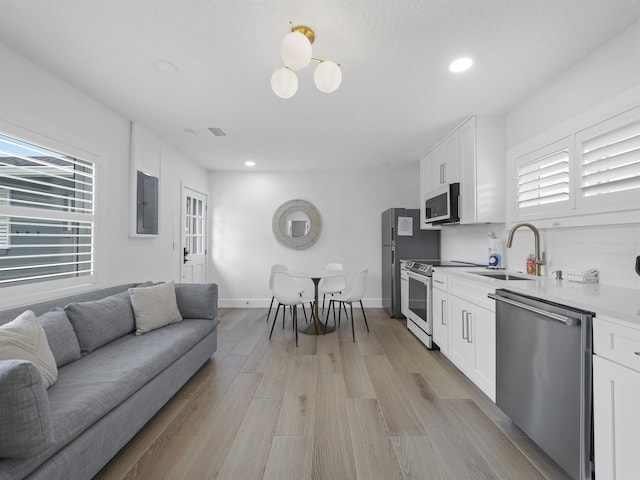 kitchen featuring electric stove, dishwasher, light wood-type flooring, white cabinetry, and a sink