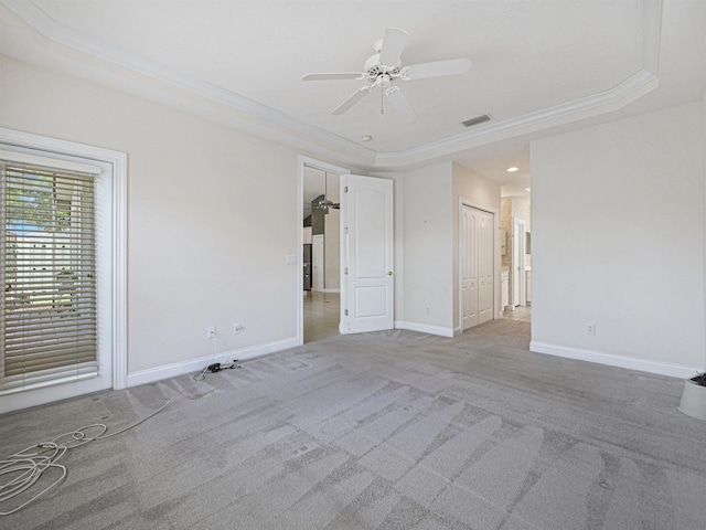 empty room with a raised ceiling, ceiling fan, and light colored carpet