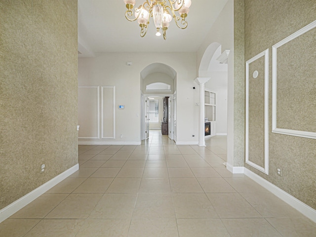 interior space featuring decorative columns, light tile patterned floors, a towering ceiling, and an inviting chandelier