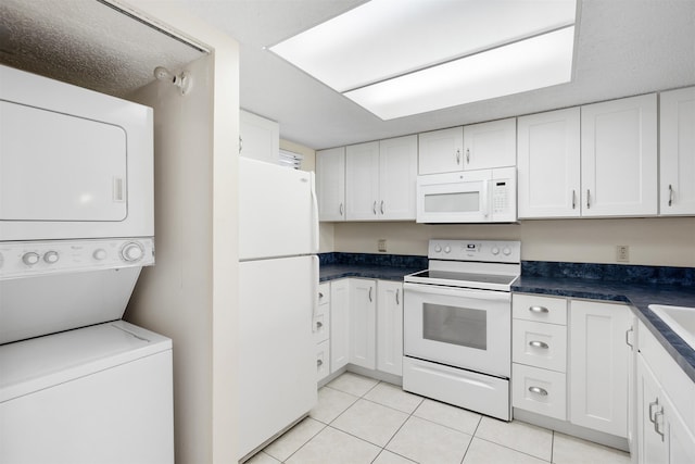 kitchen with stacked washing maching and dryer, white appliances, a textured ceiling, light tile patterned floors, and white cabinets