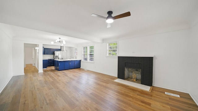 819 Mcduff Ave, Jacksonville, FL 32205 - unfurnished living room featuring ceiling fan with notable chandelier, light wood-type flooring, visible vents, a brick fireplace, and baseboards
