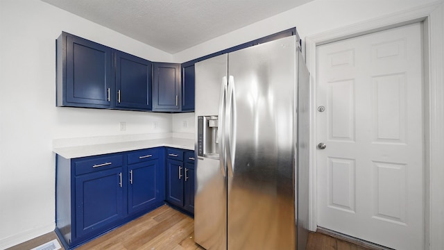 819 Mcduff Ave, Jacksonville, FL 32205 - kitchen with stainless steel fridge, a textured ceiling, light countertops, blue cabinetry, and light wood finished floors