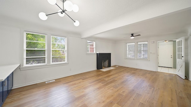 819 Mcduff Ave, Jacksonville, FL 32205 - unfurnished living room with baseboards, a fireplace, light wood-style flooring, visible vents, and ceiling fan with notable chandelier