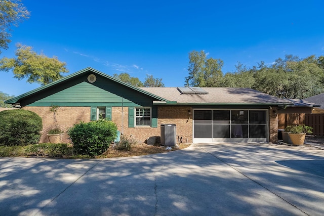 ranch-style house featuring cooling unit, roof mounted solar panels, brick siding, and driveway