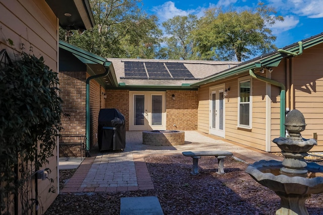 rear view of property with a patio, solar panels, brick siding, french doors, and roof with shingles