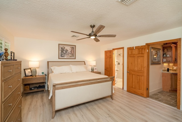 bedroom with light wood-type flooring, visible vents, and ensuite bath