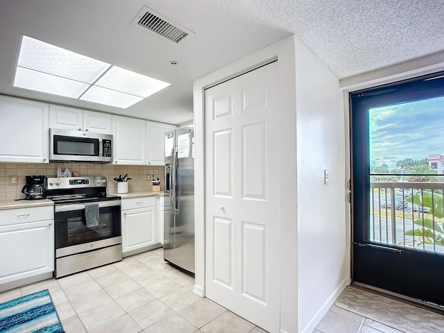 kitchen with white cabinets, appliances with stainless steel finishes, light countertops, tasteful backsplash, and visible vents
