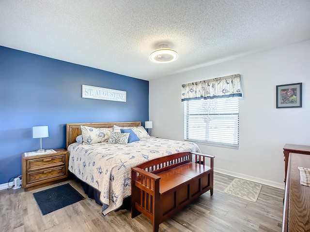 bedroom with baseboards, a textured ceiling, and wood finished floors