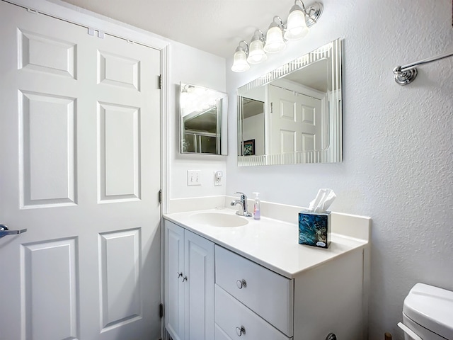 half bathroom featuring vanity, a textured wall, and toilet
