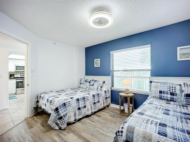 bedroom featuring baseboards, light wood-style flooring, and a textured ceiling