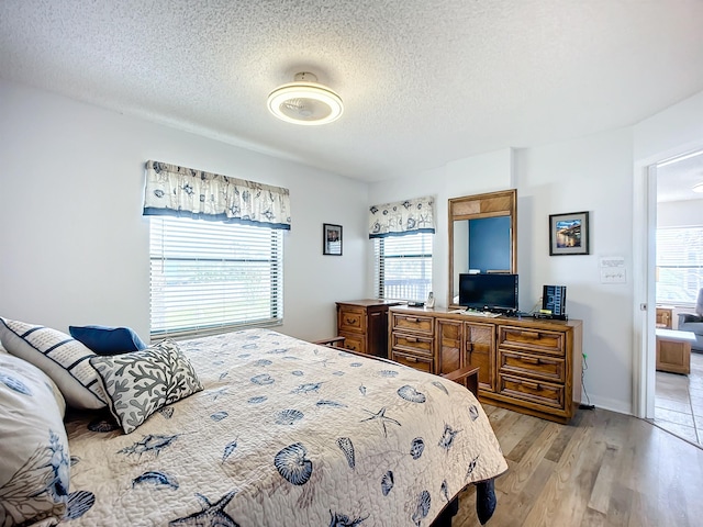 bedroom featuring multiple windows, light wood finished floors, and a textured ceiling