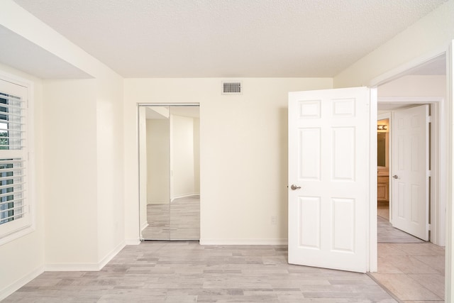 unfurnished bedroom featuring a textured ceiling, a closet, and light hardwood / wood-style flooring