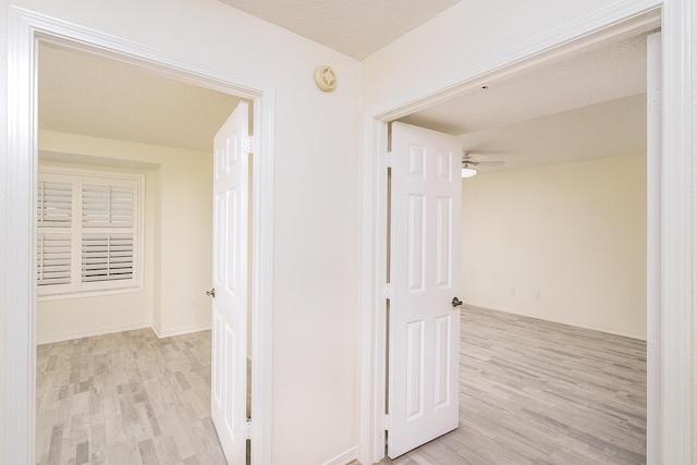 corridor with a textured ceiling and light wood-type flooring