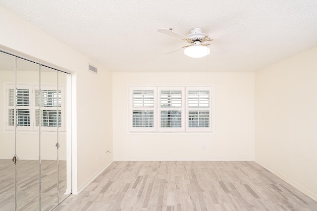 unfurnished room with ceiling fan, a textured ceiling, and light wood-type flooring