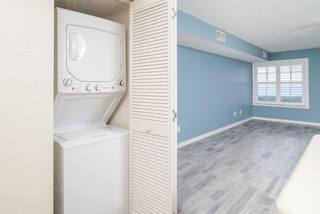 clothes washing area featuring stacked washer and dryer, light hardwood / wood-style flooring, and a textured ceiling