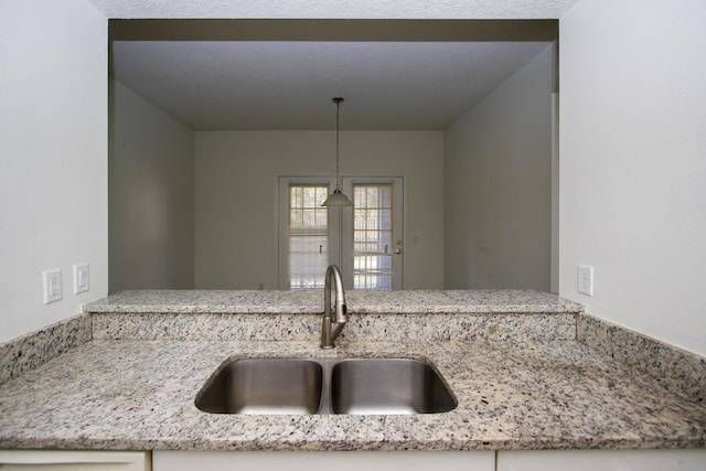 kitchen with decorative light fixtures, light stone counters, and sink