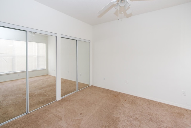 unfurnished bedroom featuring ceiling fan, light carpet, and two closets