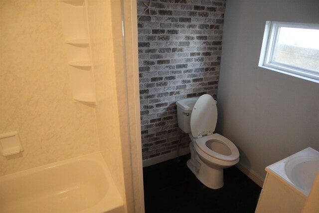 bathroom with sink, toilet, a tub, and brick wall