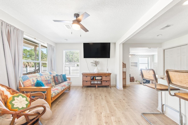 living room featuring a textured ceiling, light wood-type flooring, and ceiling fan