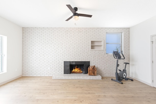 workout area featuring a brick fireplace, brick wall, and light wood-type flooring