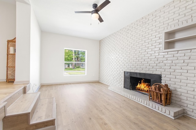 unfurnished living room featuring ceiling fan, light wood-type flooring, a fireplace, and brick wall