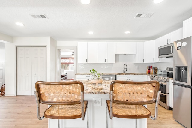 kitchen with light stone countertops, appliances with stainless steel finishes, light wood-type flooring, and white cabinetry