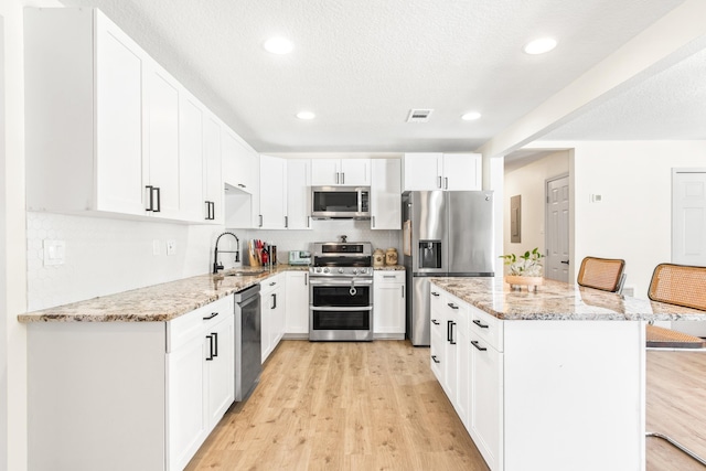 kitchen with light stone countertops, appliances with stainless steel finishes, sink, white cabinetry, and a breakfast bar area