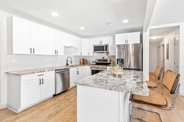 kitchen featuring sink, light stone counters, light hardwood / wood-style floors, white cabinets, and appliances with stainless steel finishes