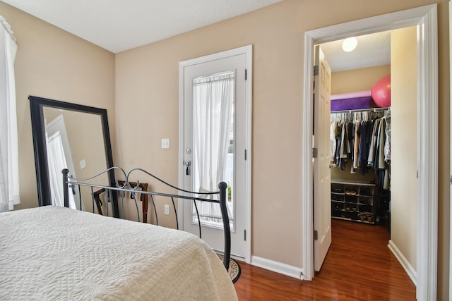 bedroom featuring wood finished floors, a closet, a walk in closet, and baseboards