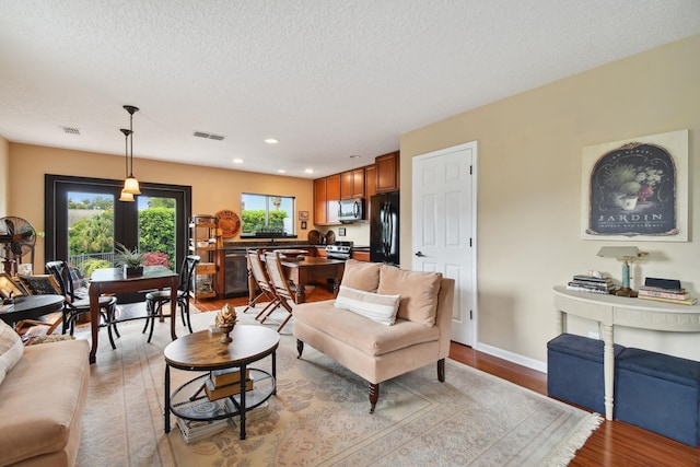 living area with a textured ceiling, wood finished floors, and visible vents