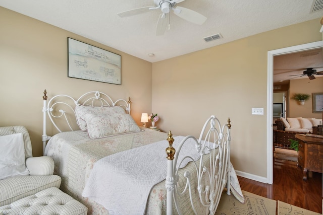 bedroom with a textured ceiling, wood finished floors, a ceiling fan, visible vents, and baseboards