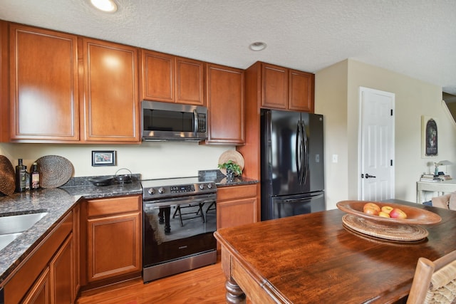 kitchen with stainless steel appliances, brown cabinetry, light wood-style floors, and a textured ceiling