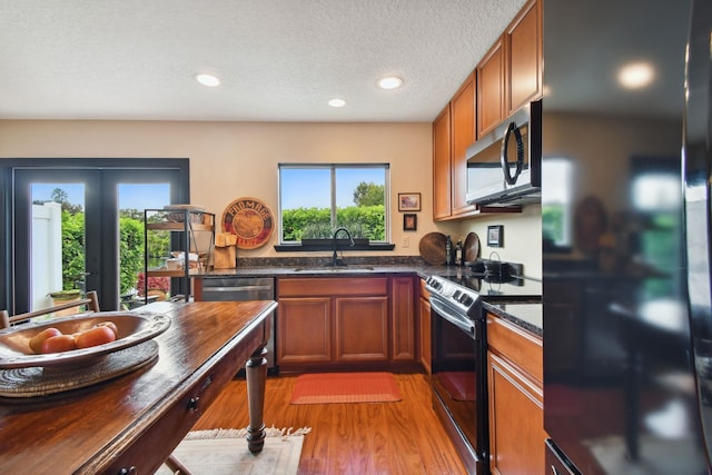 kitchen featuring brown cabinets, a textured ceiling, light wood-type flooring, black appliances, and a sink