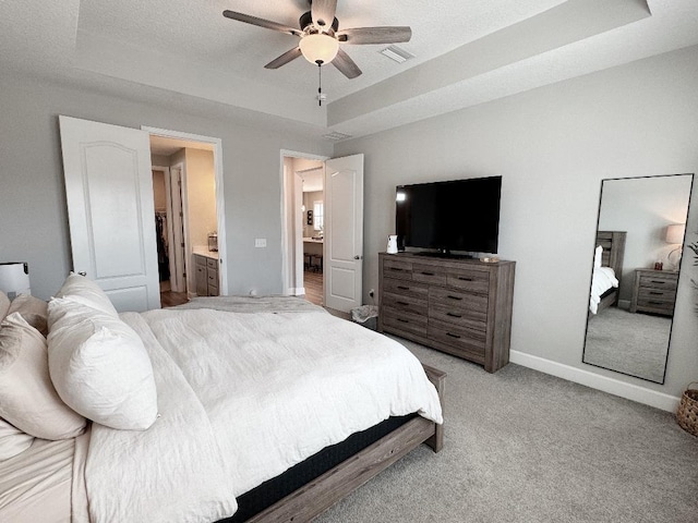 carpeted bedroom with a raised ceiling, ceiling fan, a textured ceiling, and ensuite bath