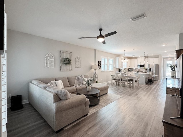 living room with hardwood / wood-style flooring, ceiling fan with notable chandelier, and a textured ceiling